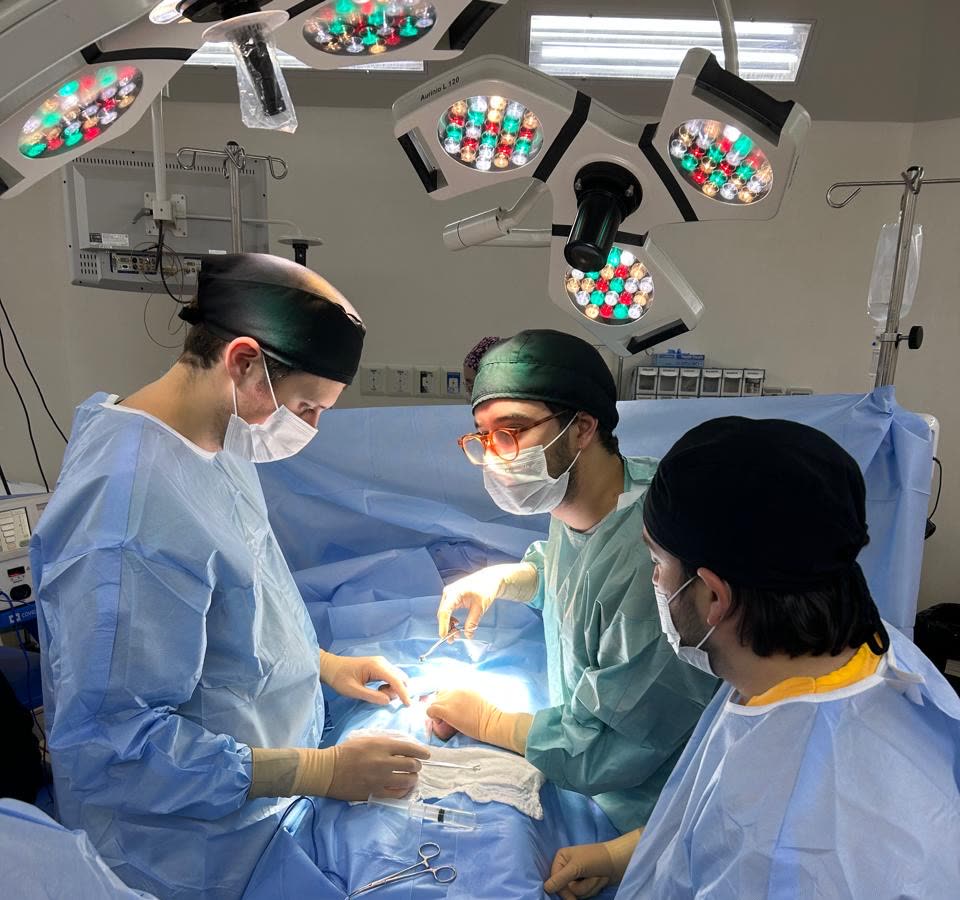 Tres cirujanos trabajando concentrados bajo la lámpara de pabellón